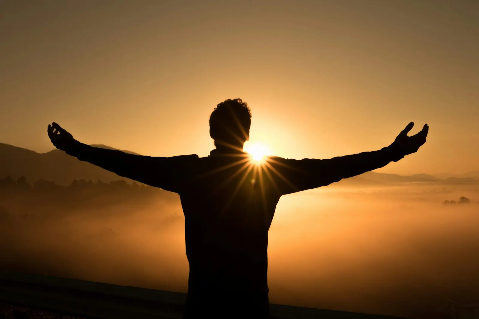 Silhouette of a person with arms outstretched at sunrise